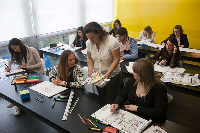 Allievi in aula al lavoro su un progetto d'interior design con campionari e materiali